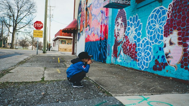 Boy wearing blue hoodie taking photograph of a wall of art